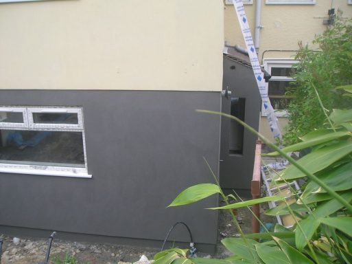 Side view of a house with a grey rendered wall and a ladder nearby.
